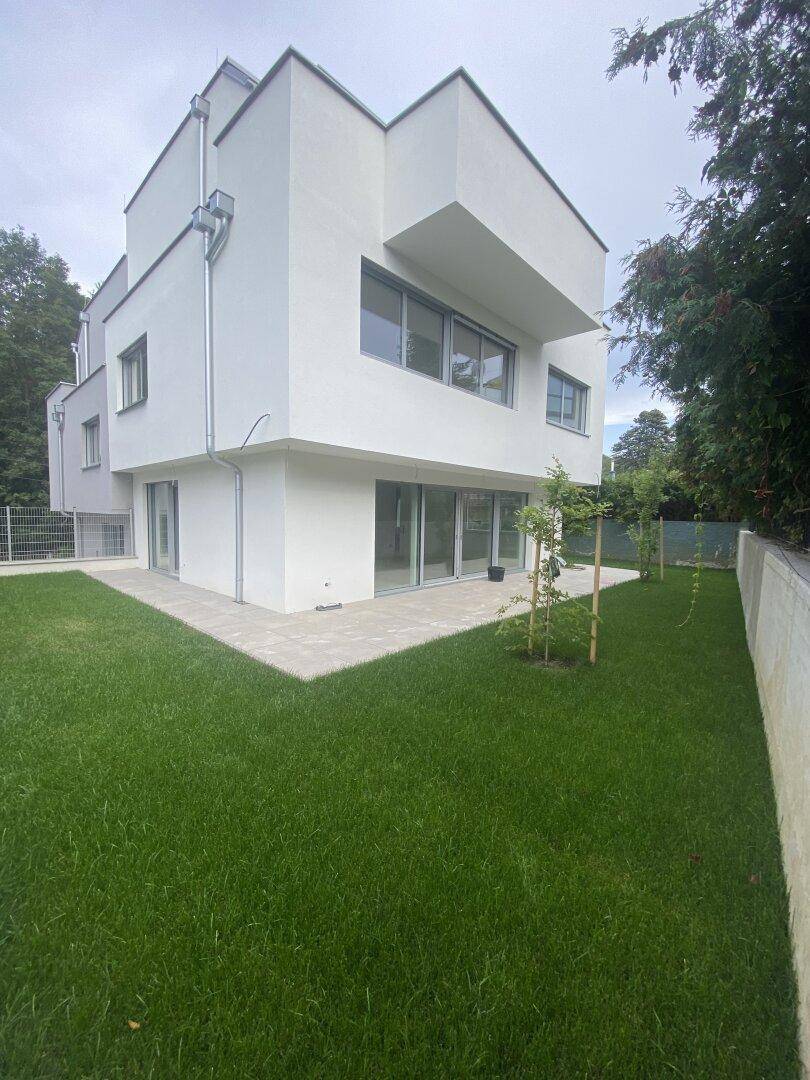 Moderner Neubau mit weißer Fassade, umgeben von einem frisch angelegten Rasen und einer kleinen Terrasse.