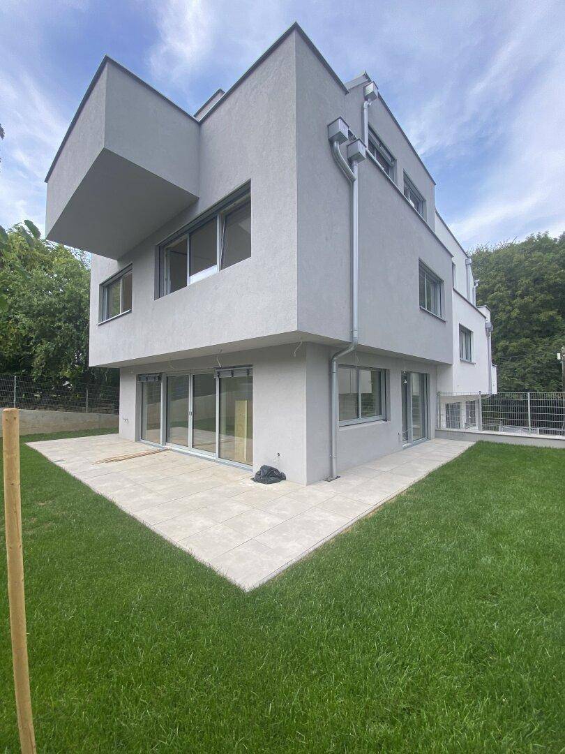 Moderner Neubau mit grauer Fassade, umgeben von einem gepflegten Rasen und einer großzügigen Terrasse.