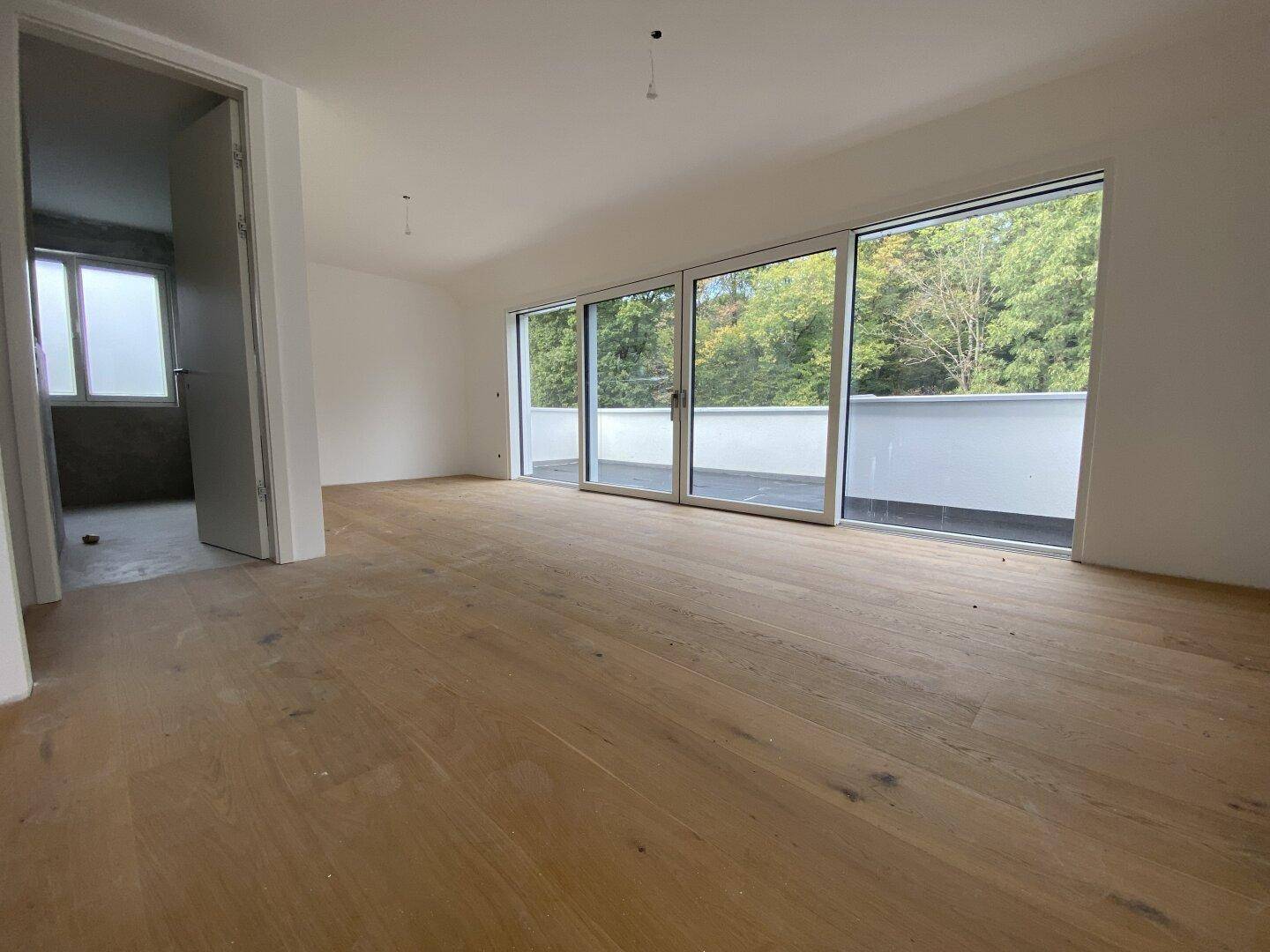 Heller Wohnbereich mit Holzboden und großen Schiebetüren, die Zugang zu einem Balkon bieten.