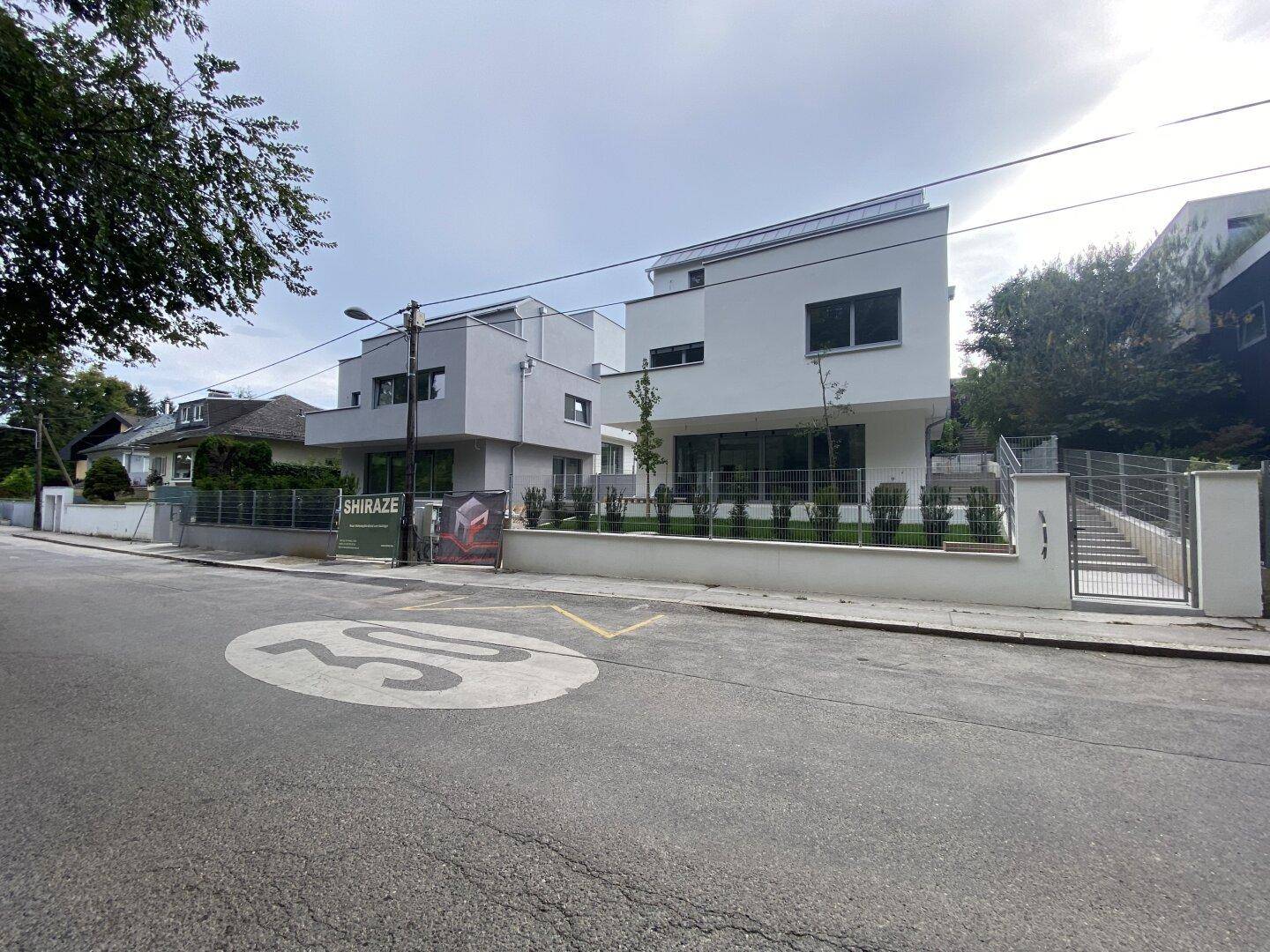Zwei moderne Neubauten mit weißer Fassade und großen Fenstern, gesehen von der Straße mit Geschwindigkeitsbegrenzung.