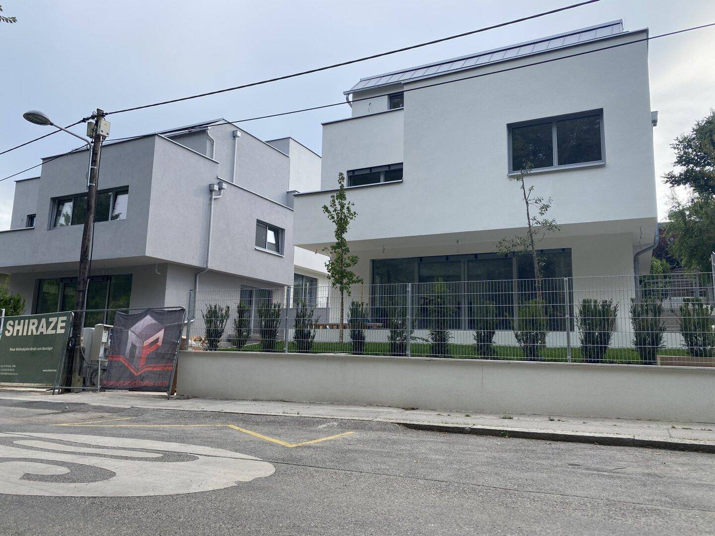 Moderne weiße und graue Neubauten mit großen Fenstern und gepflegten Vorgärten an einer ruhigen Straße.