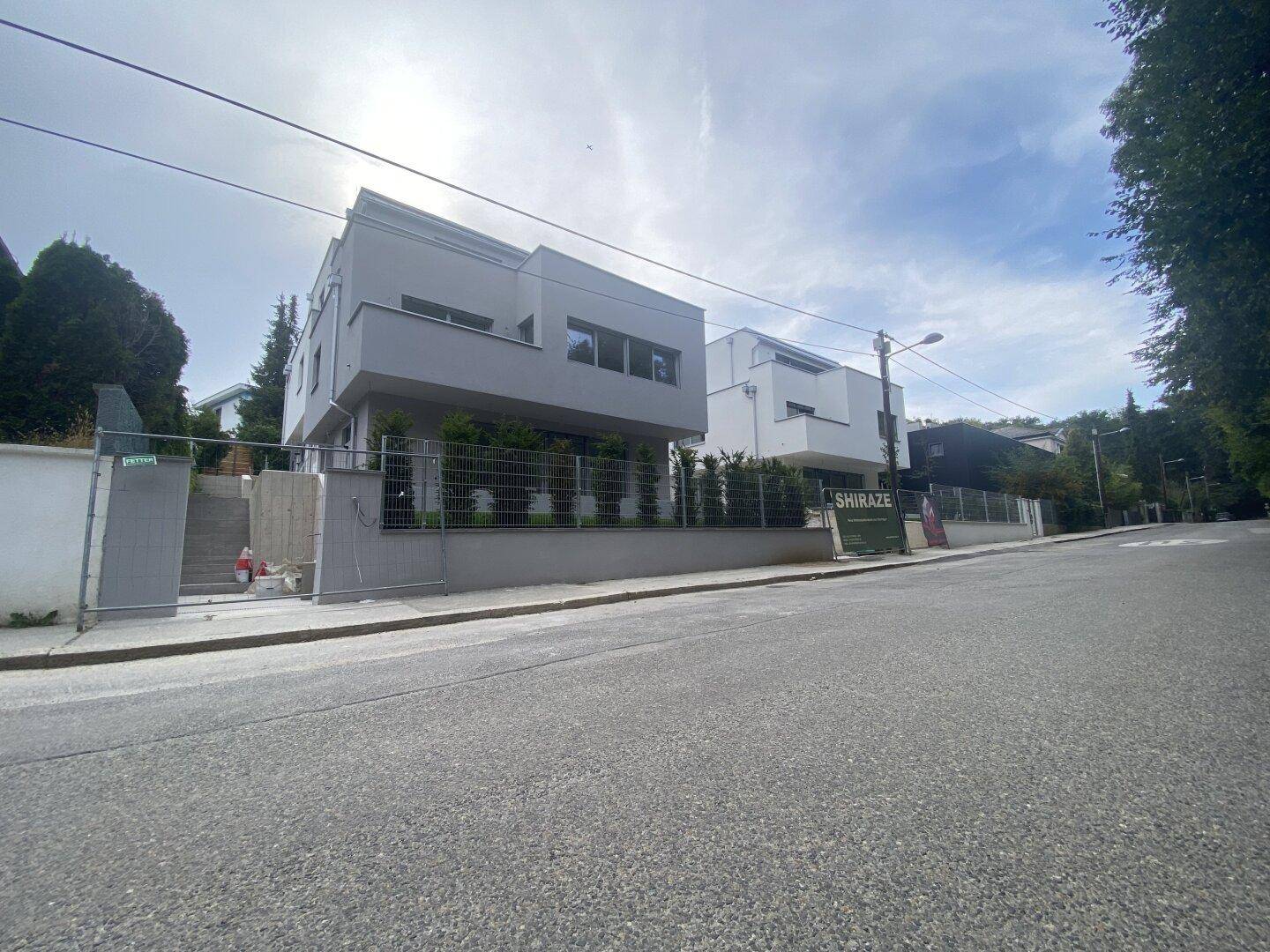 Seitenansicht eines modernen grauen Gebäudes von der Straße aus mit angrenzendem weißen Neubau.