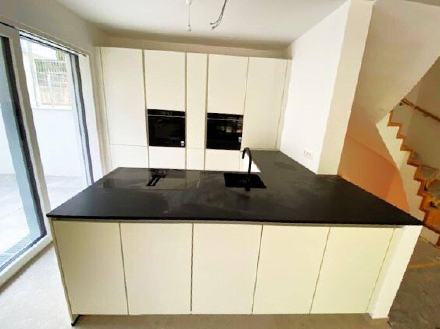 Moderne Einbauküche mit weiß-matten Fronten, schwarzer Arbeitsplatte und integrierten Geräten.