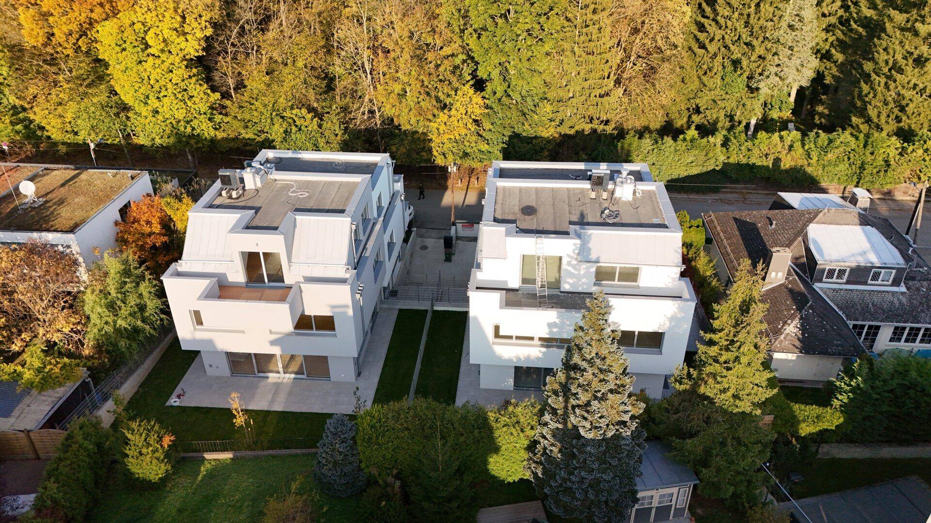 Luftaufnahme von zwei modernen Wohngebäuden mit Flachdächern und umgebender grüner Landschaft.