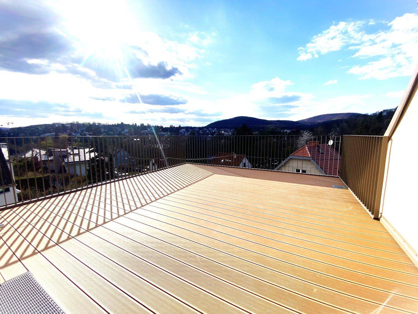 Helle Dachterrasse mit Holzboden und Panoramablick auf die umliegende grüne Hügellandschaft.