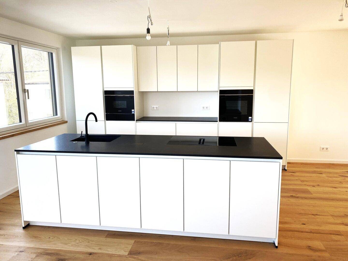 Elegante weiße Küche mit langer Kochinsel und integrierten Backöfen, ideal für offenes Wohnen.