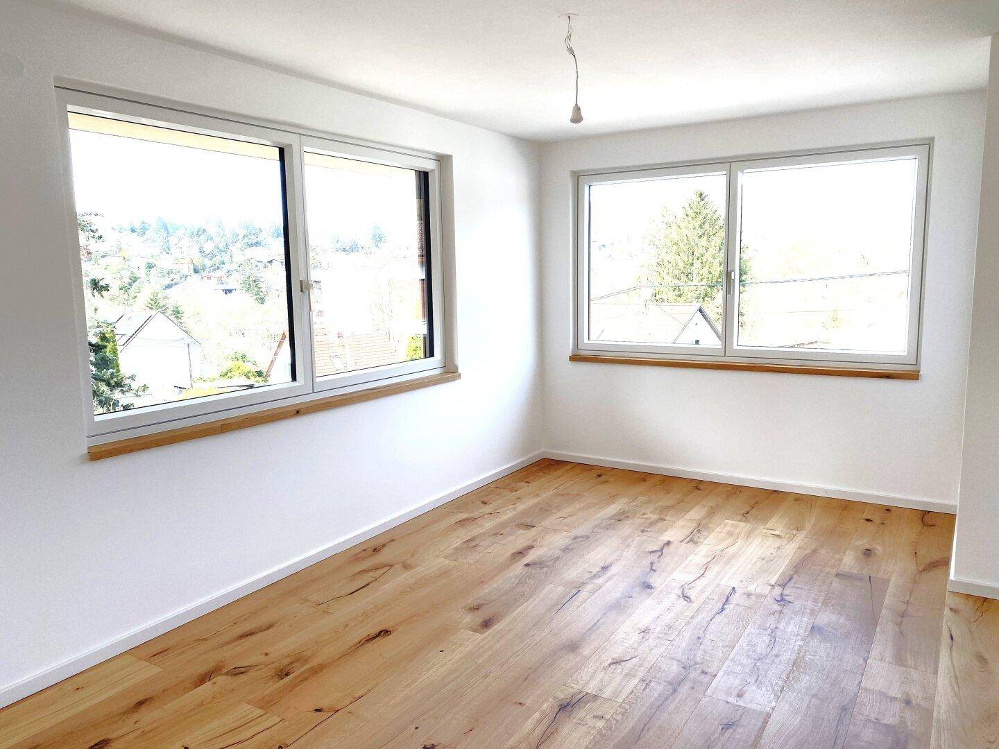 Helles Schlafzimmer mit neuem Holzparkettboden und weitem Blick ins Grüne durch große Fenster.