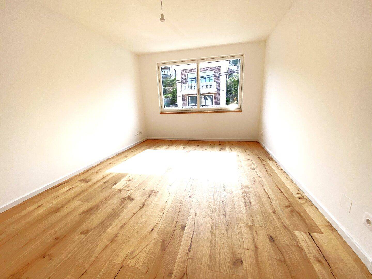 Lichtdurchfluteter Raum mit elegantem Holzparkett und einem Fenster mit Blick auf die Umgebung.
