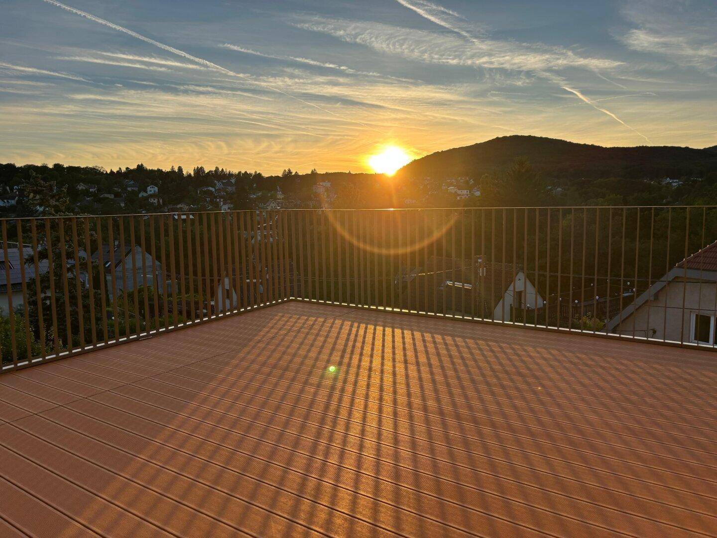 Geräumige Dachterrasse mit Holzboden und weitem Blick über die Landschaft bei Sonnenuntergang.