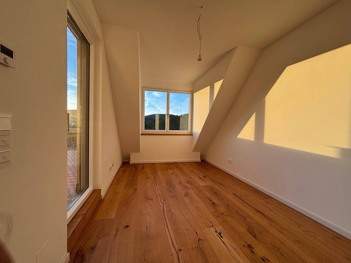 Sonniger Raum im Dachgeschoss mit Holzparkett und Zugang zu einer Terrasse oder Balkon.