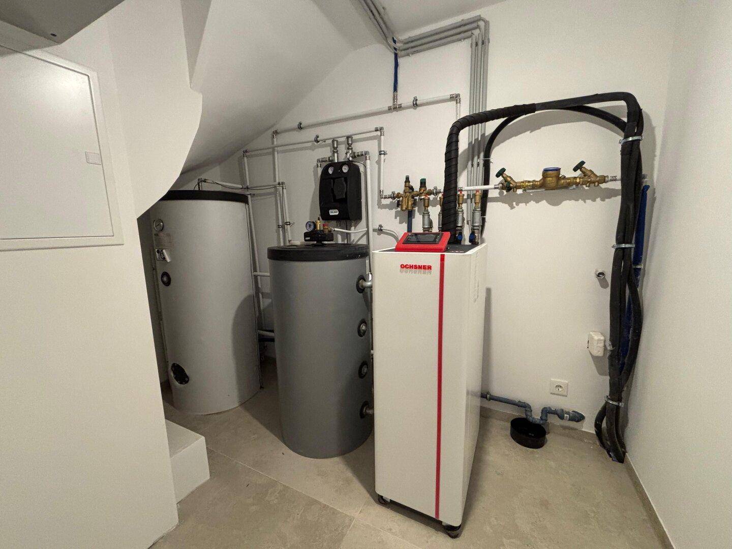 Technikraum mit moderner Ochsner Wärmepumpe und zwei Warmwasserspeichern unter Dachschräge.