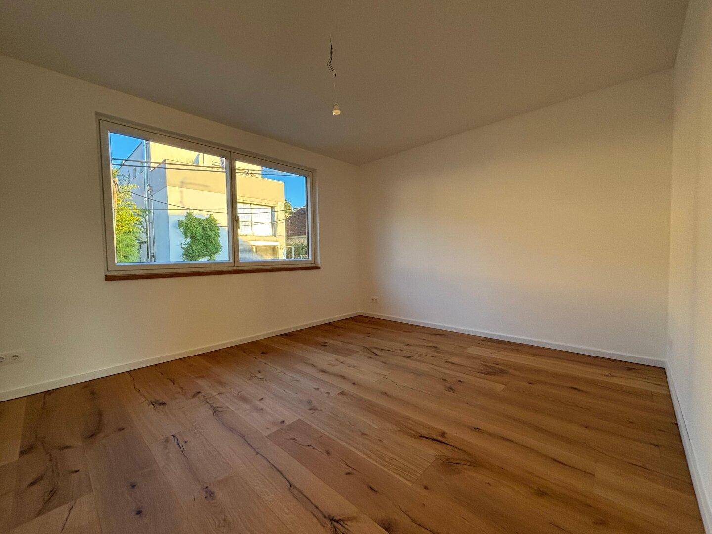 Helles Zimmer mit breiten Holzplankenboden und großem Fenster, bereit zum Einrichten.