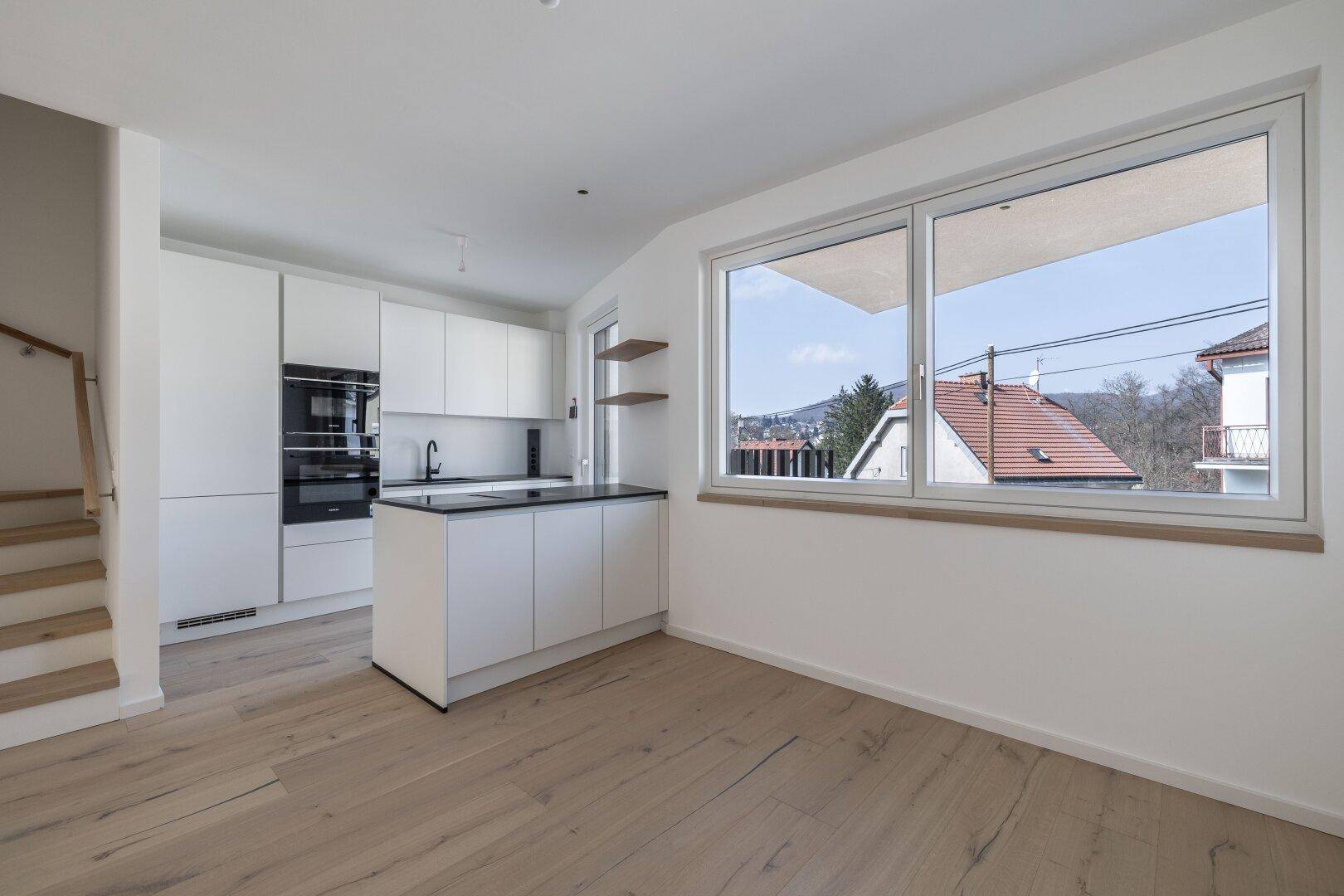 Moderne Einbauküche mit weißen Schränken, dunkler Arbeitsplatte und großem Fenster mit Ausblick.