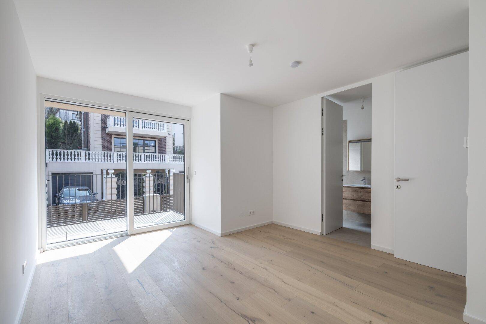 Helles Schlafzimmer mit Holzboden, großem Fenster und direktem Zugang zu einem modernen Badezimmer.