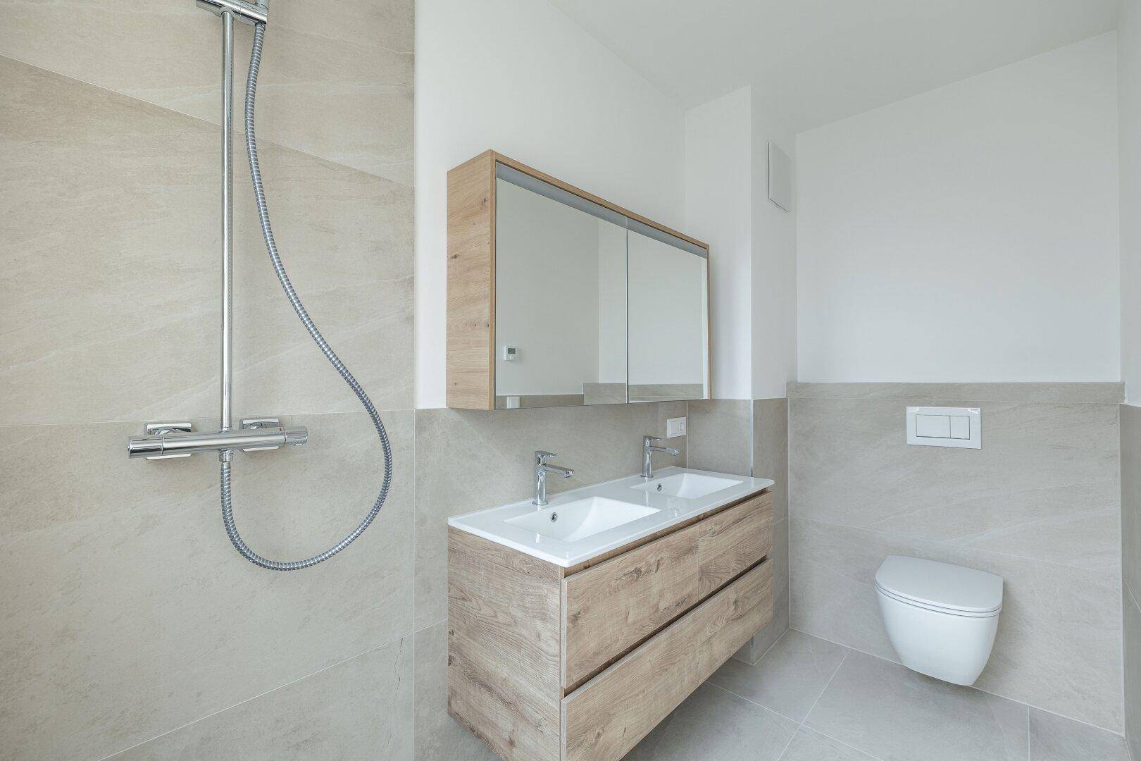 Modernes Badezimmer mit Doppelwaschbecken, begehbarer Dusche und hellen Fliesen an den Wänden.