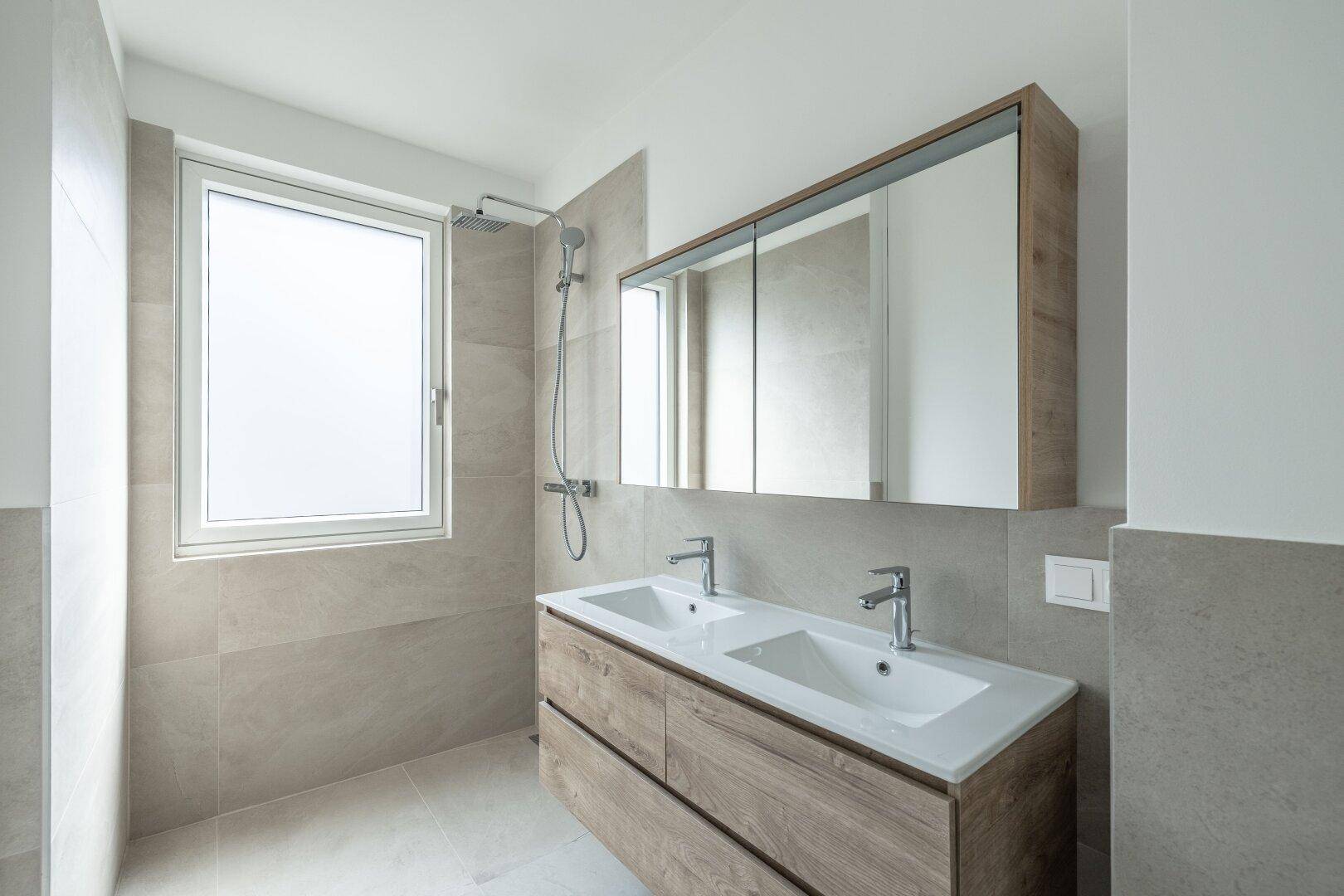 Helles, modernes Badezimmer mit Doppelwaschbecken, Dusche und Fenster für natürliche Belüftung.