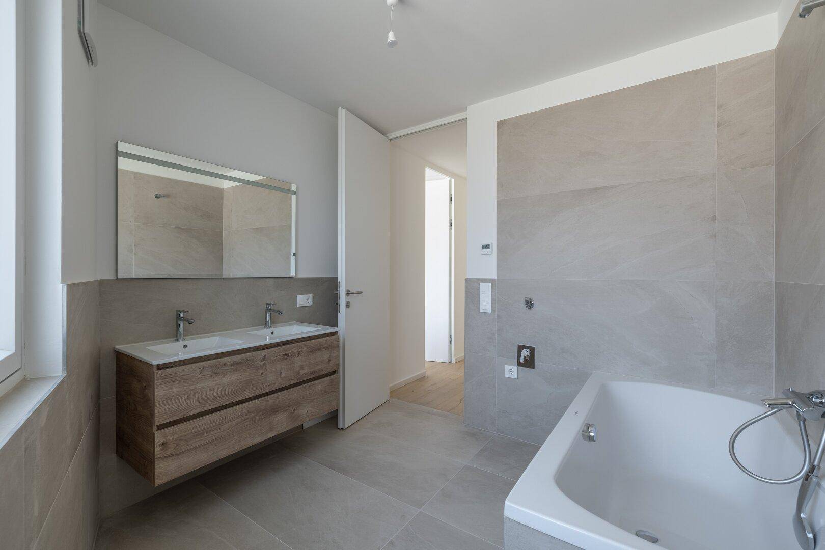 Geräumiges Badezimmer mit Badewanne, Doppelwaschbecken und Zugang zu einem angrenzenden Raum.