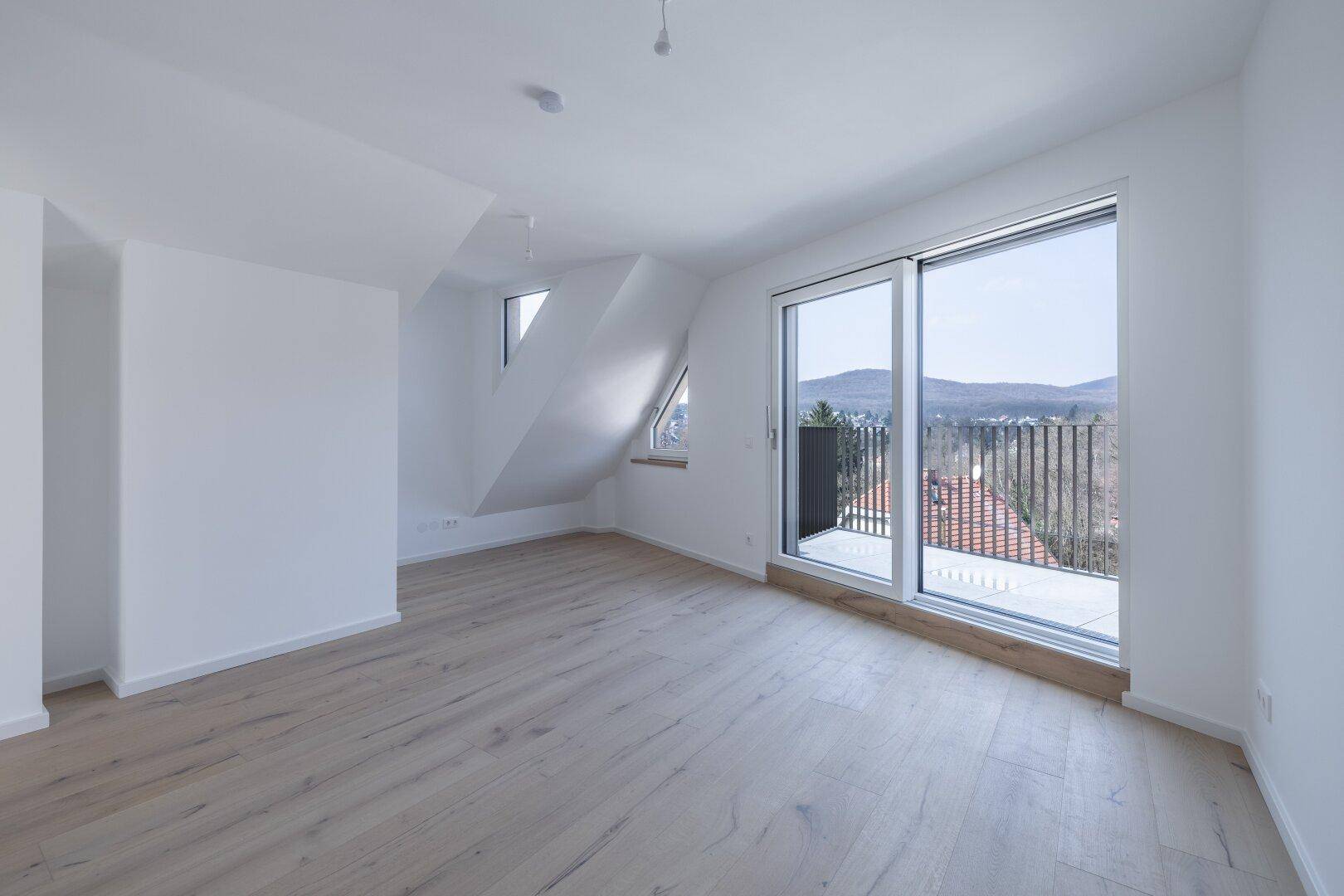 Helles Dachgeschosszimmer mit Holzboden, Balkonzugang und weitem Panoramablick über die Landschaft.