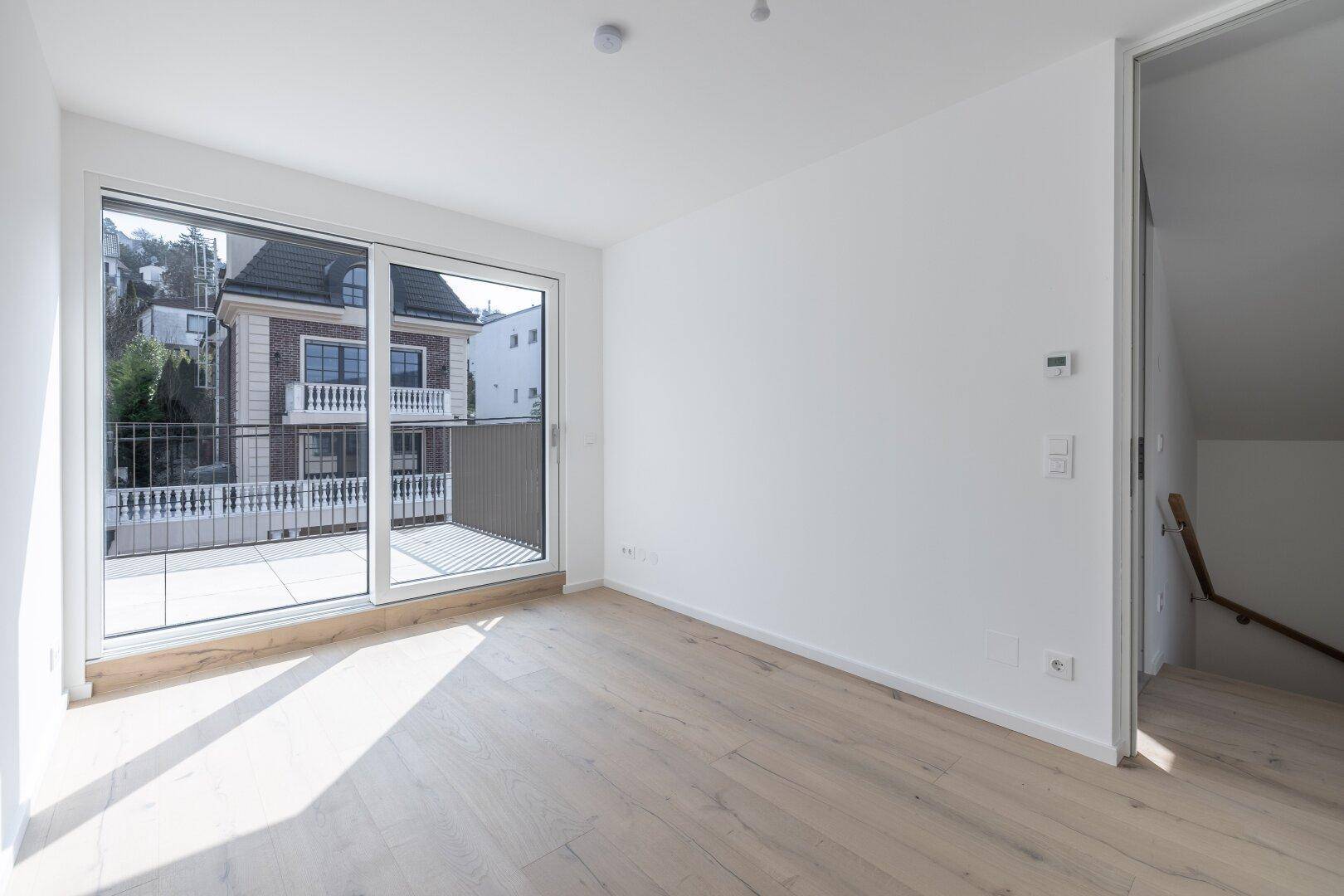 Helles Zimmer mit Holzboden, großem Fenster und direktem Zugang zu einem sonnigen Balkon.