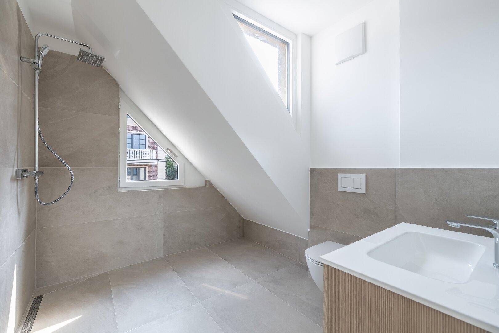 Modernes Dachgeschoss-Badezimmer mit Dusche, Wand-WC und Waschtisch unter einer Dachschräge.