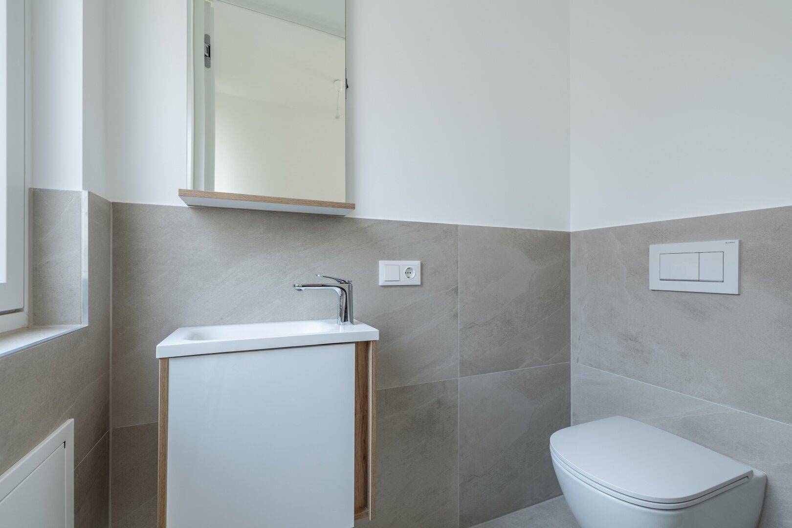 Kleines, modernes Gäste-WC mit Waschtisch, Wand-WC und hellen Fliesen an den Wänden.