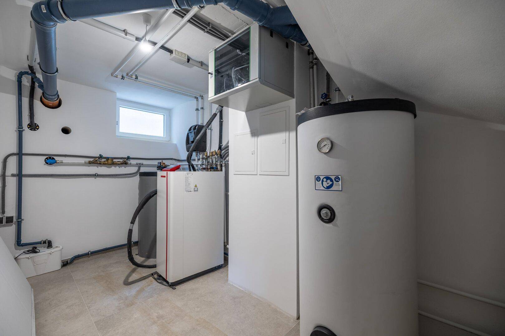 Technikraum mit Heizungsanlage, Warmwasserspeicher und sichtbaren Installationen.