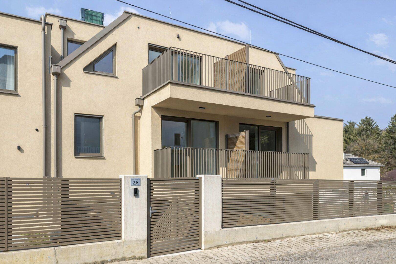 Zeitgenössisches Wohngebäude mit beiger Fassade, Balkonen und einem modernen Zaun an der Straße.