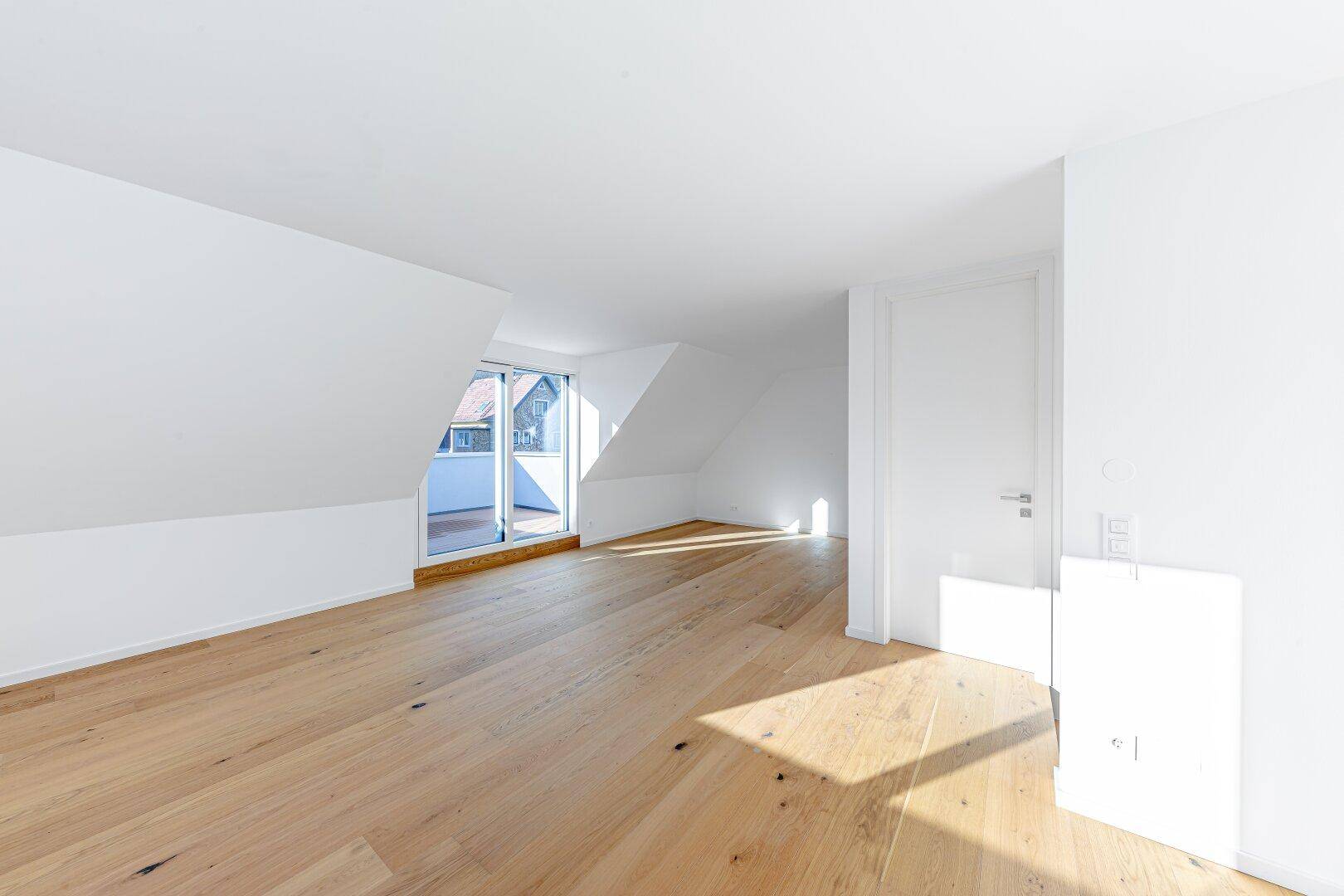 Helles Schlafzimmer im Dachgeschoss mit Holzboden und Zugang zu einem kleinen Balkon.