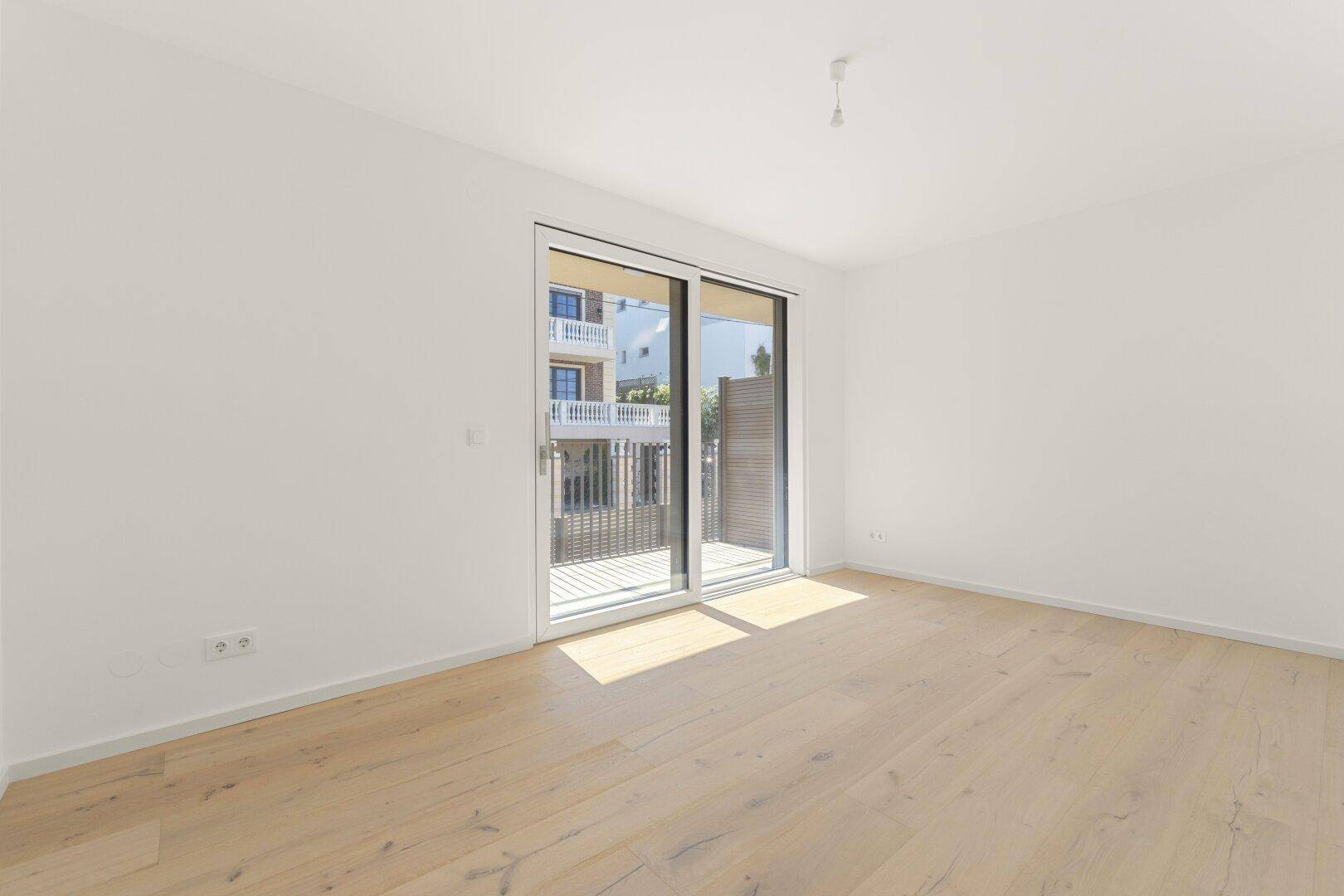 Helles Schlafzimmer mit Holzboden und großem Schiebetür-Zugang zu einem Balkon.