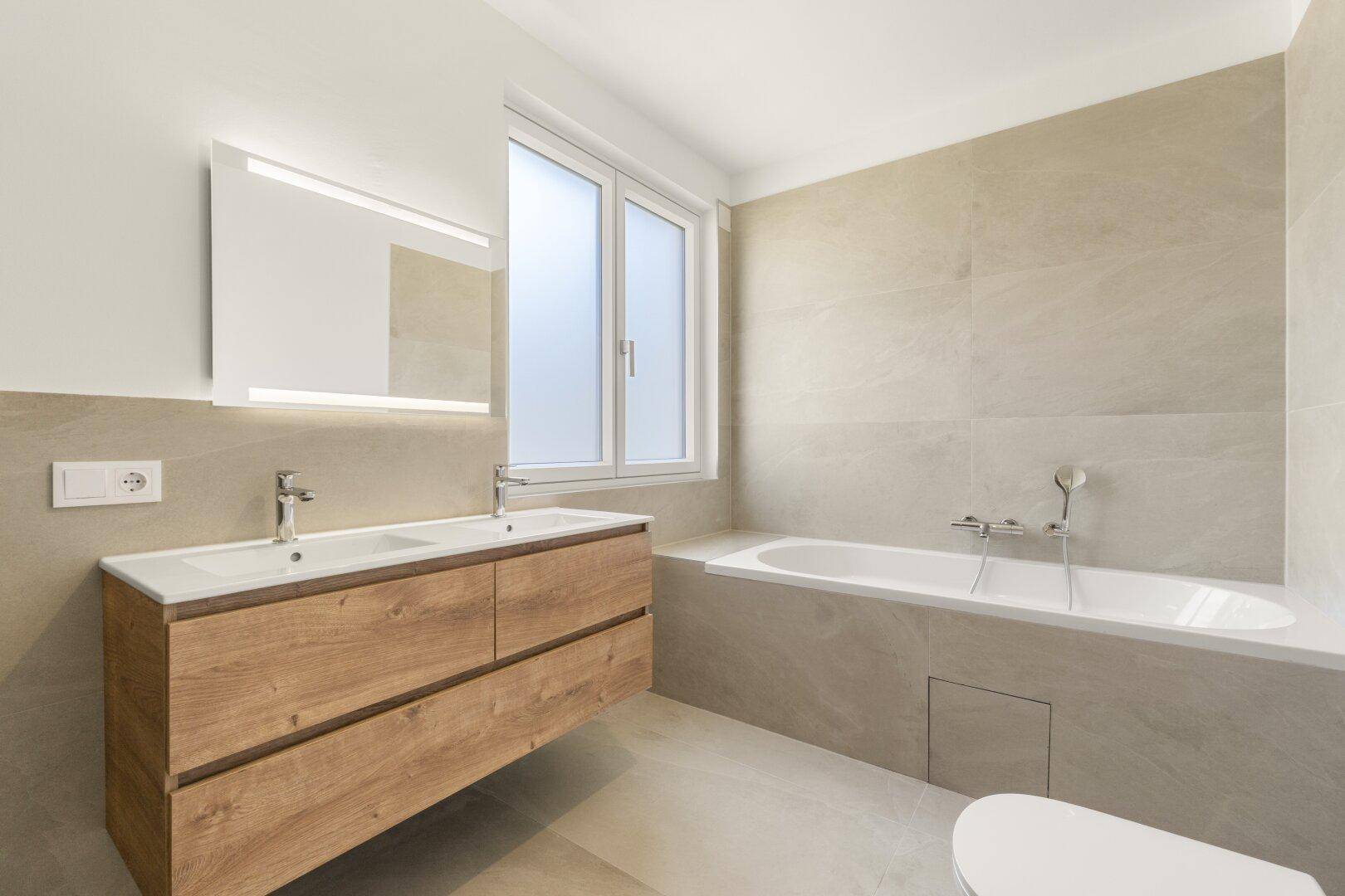 Modernes Badezimmer mit Doppelwaschbecken, Holzunterschrank, Badewanne und großen Fliesen.
