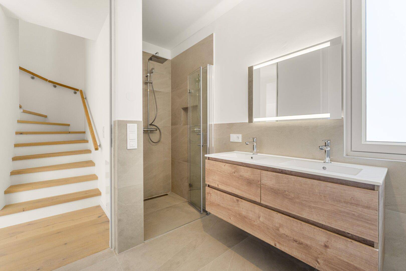 Elegantes Badezimmer mit Doppelwaschbecken, begehbarer Dusche und Zugang zum Treppenhaus.