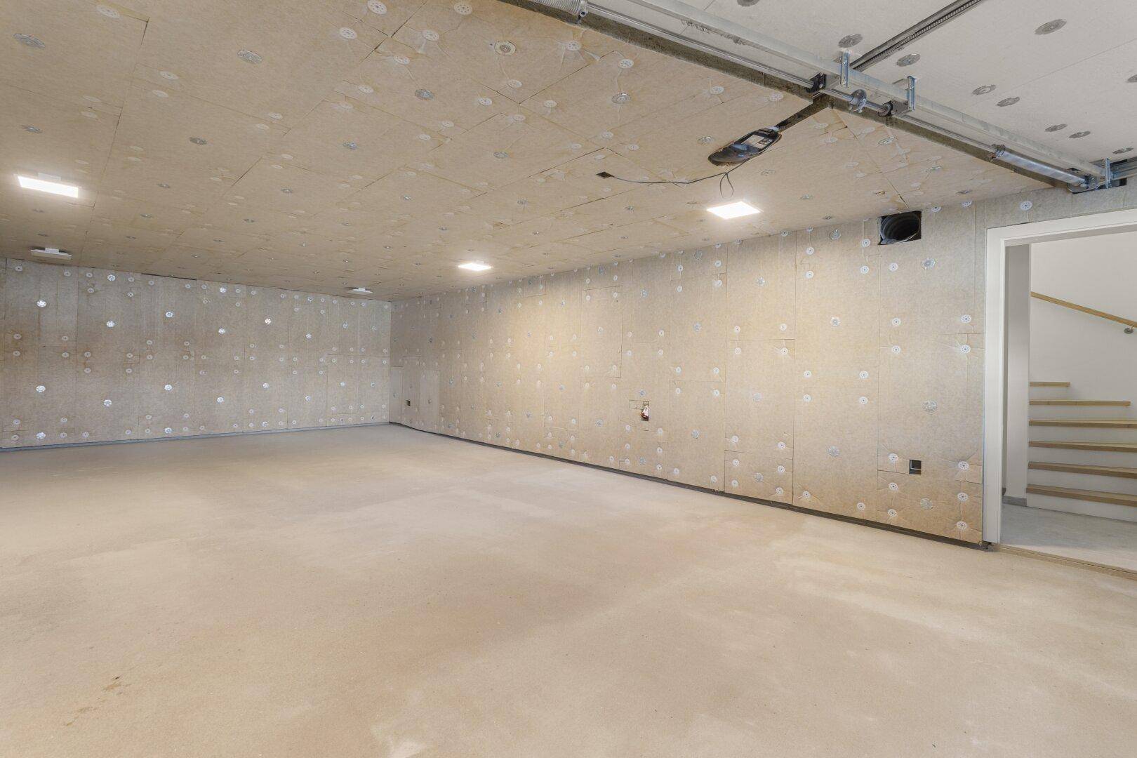 Geräumiger Kellerraum mit Betonboden und Zugang zum oberen Stockwerk über eine Treppe.