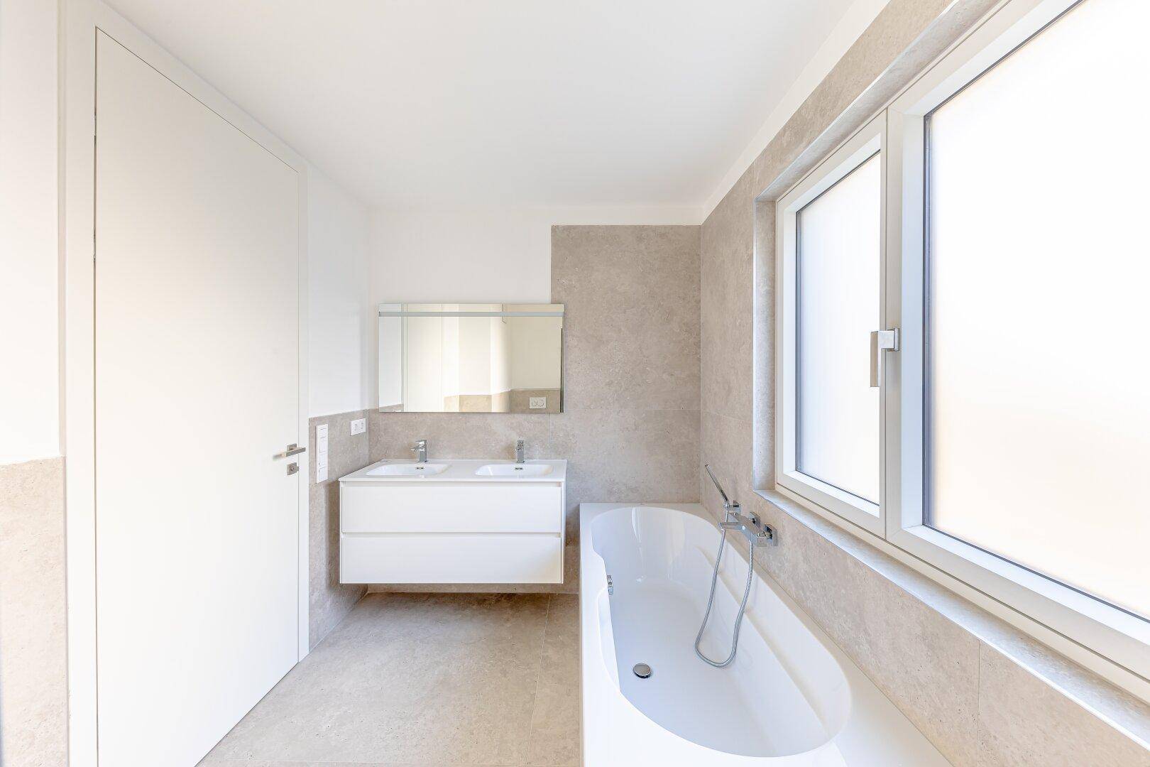 Modernes Badezimmer mit Doppelwaschbecken, Badewanne und großem Fenster für viel Tageslicht.