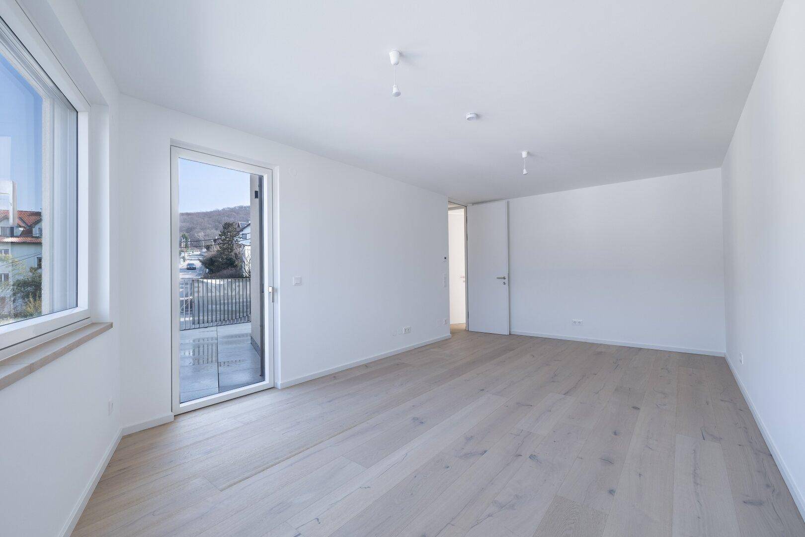 Geräumiger Wohnbereich mit hellem Holzboden und direktem Zugang zu einem Balkon, ideal für entspannte Stunden.