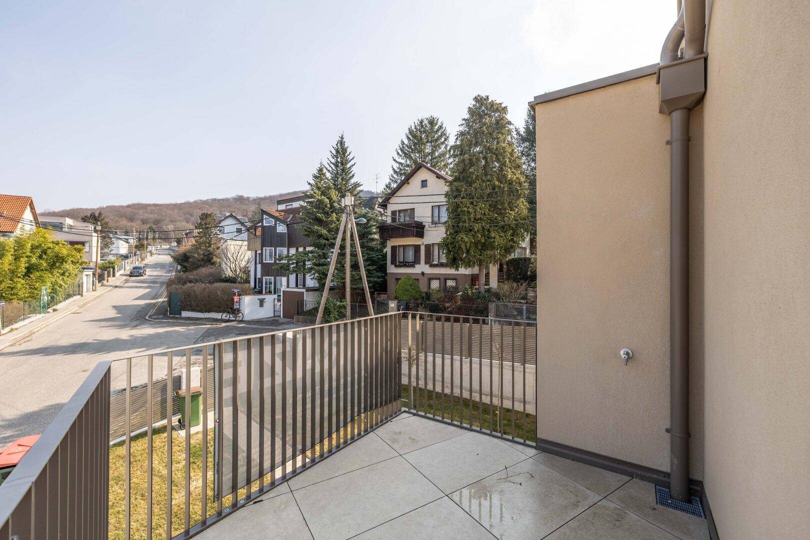 Heller Balkon mit modernem Geländer und weitem Blick über die grüne Umgebung und die Straße.