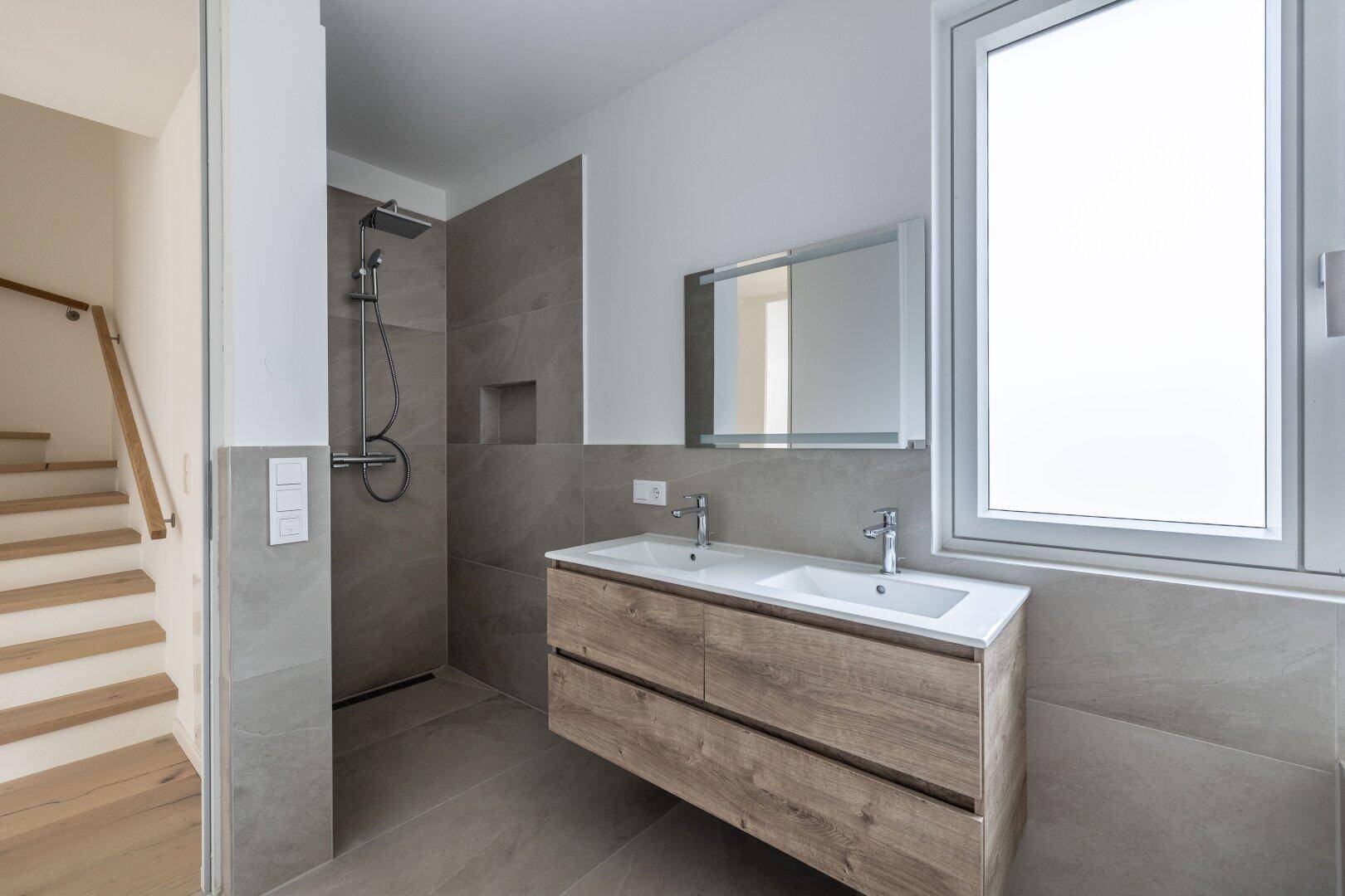 Elegantes Badezimmer mit begehbarer Dusche, Doppelwaschbecken und Holzunterschrank, hell und modern gestaltet.