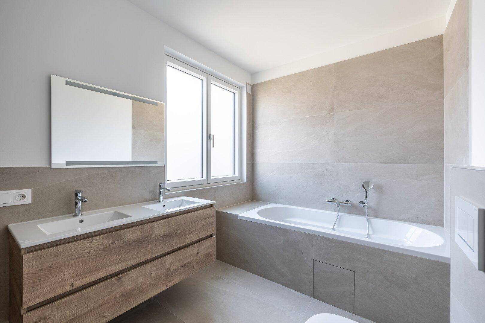 Geräumiges Badezimmer mit Doppelwaschbecken, großer Badewanne und Fenster für natürliches Licht.