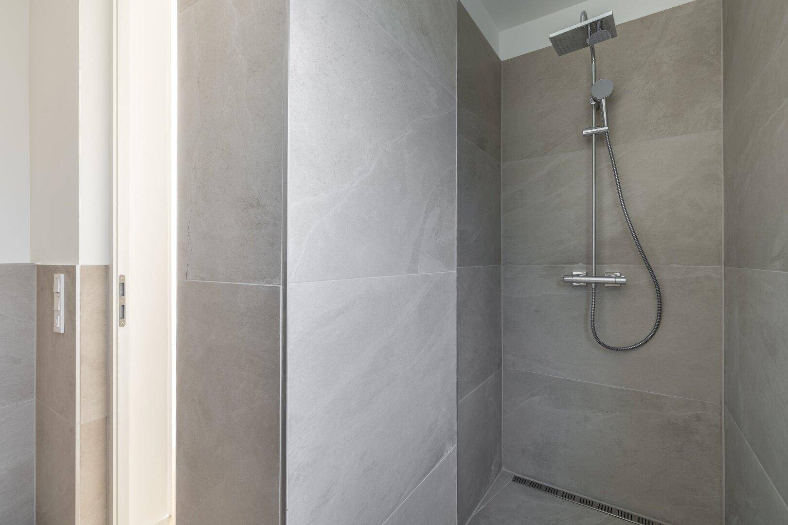 Geräumige begehbare Dusche mit Regenduschkopf und modernen hellgrauen Fliesen, sehr stilvoll.