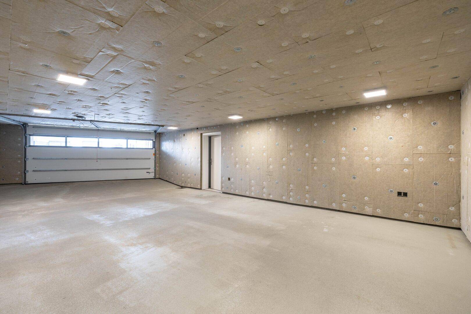 Geräumige Tiefgarage mit Rolltor und viel Platz für Fahrzeuge, noch im Ausbauzustand.
