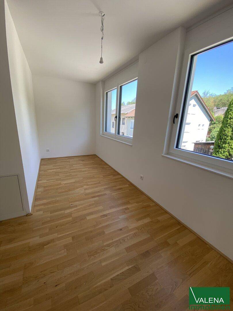 Leeres Zimmer mit Holzboden und mehreren Fenstern, bietet einen grünen Ausblick.