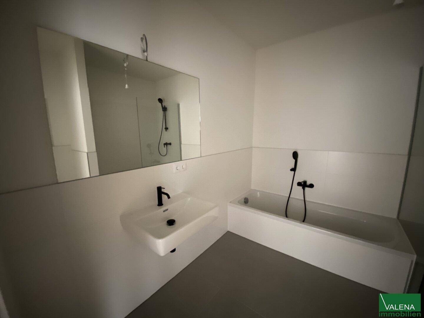 Modernes Badezimmer mit Badewanne, Waschbecken, großem Spiegel und schwarzen Armaturen.