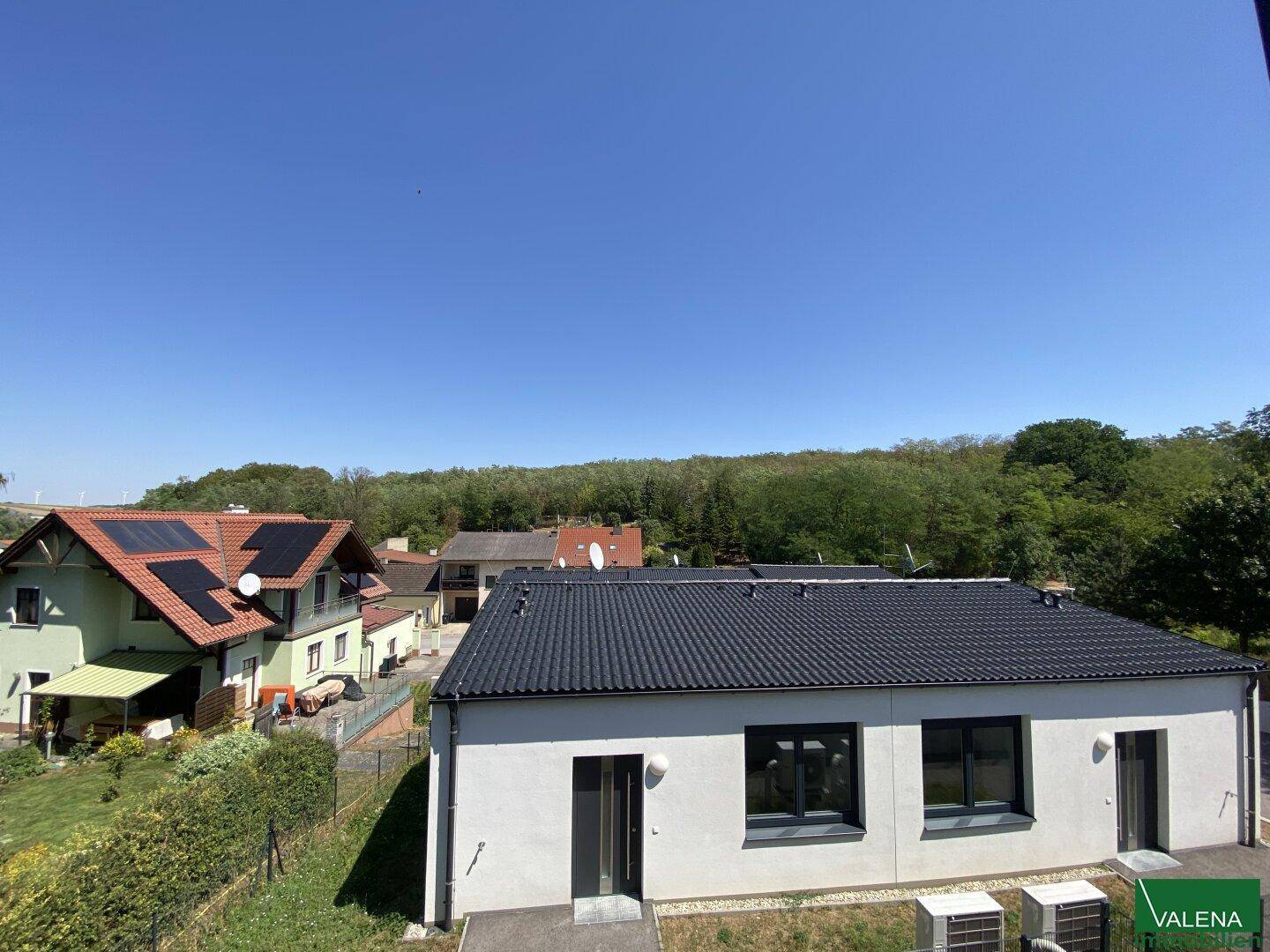 Neubau in ländlicher Umgebung mit Blick auf benachbarte Häuser und viel Grün.