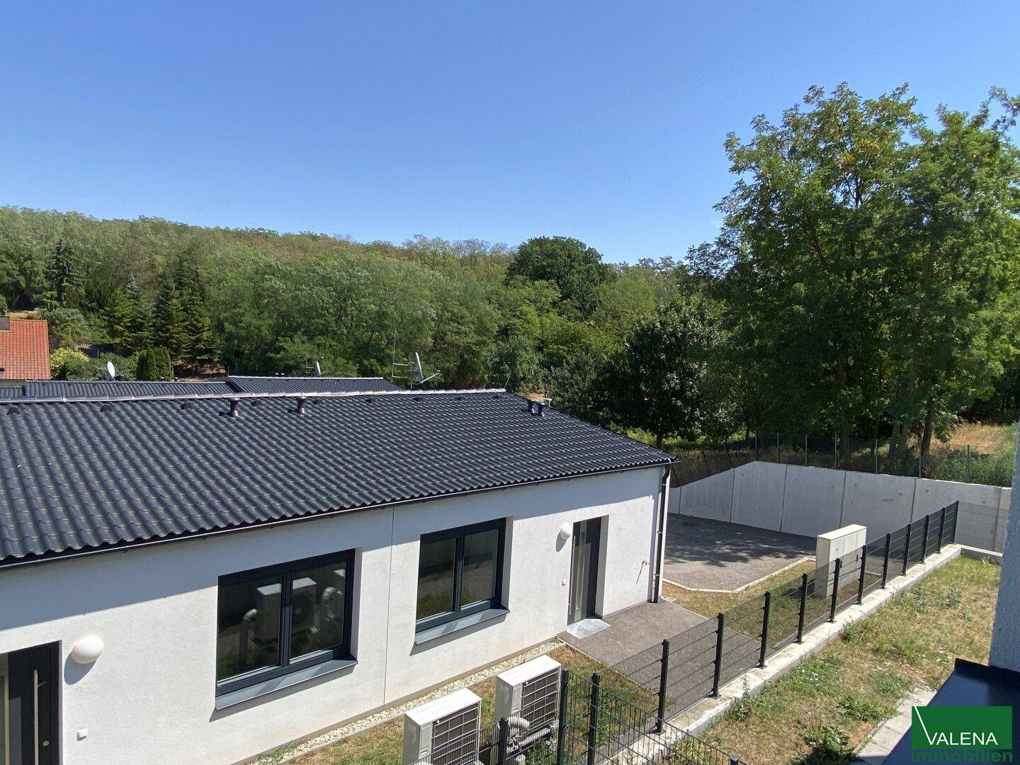 Neubau mit dunklem Dach und Blick auf grüne Bäume und die umliegende Landschaft.