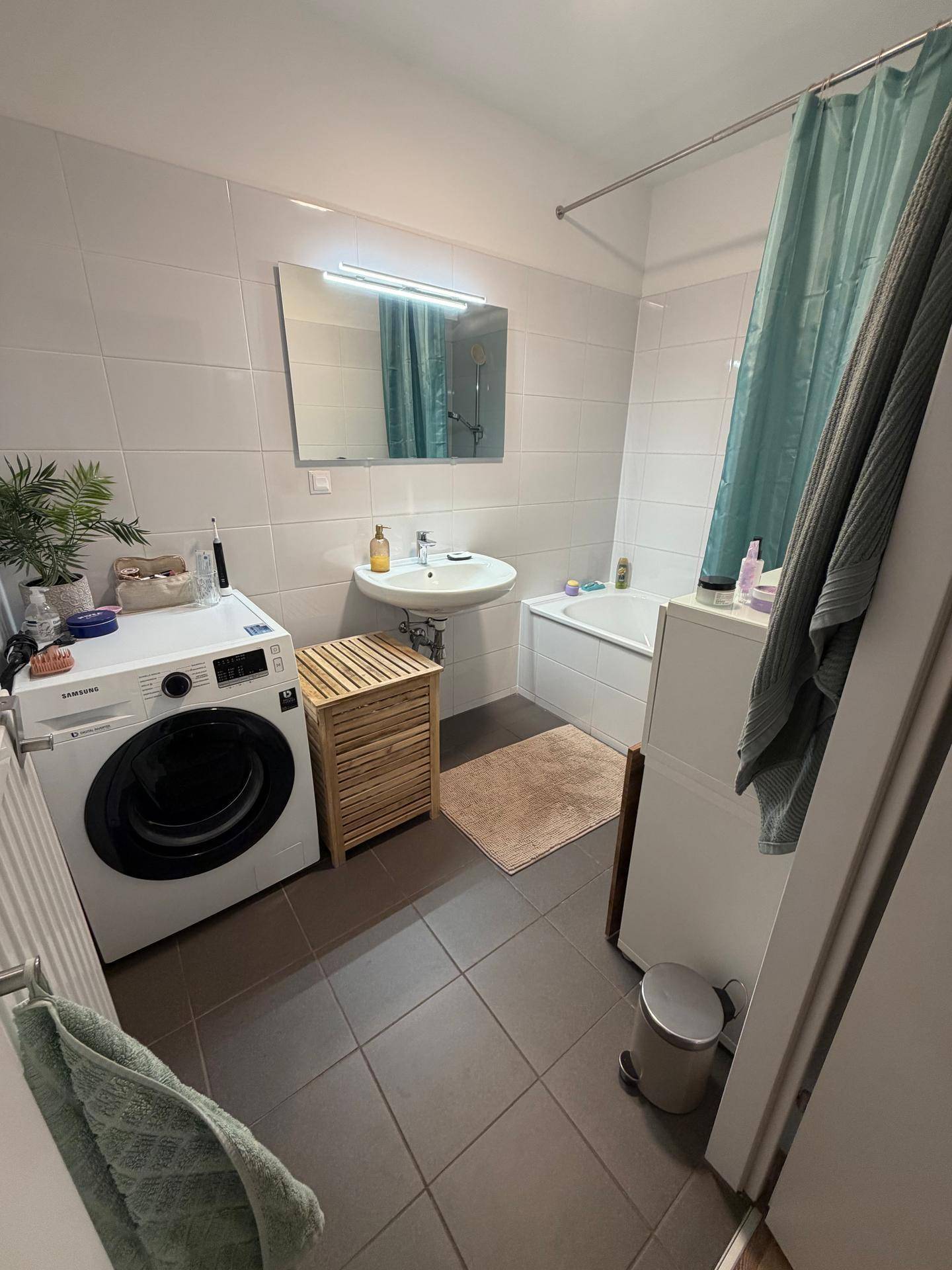 Modernes Badezimmer mit Badewanne, Waschbecken, Waschmaschine und hellen Fliesen.