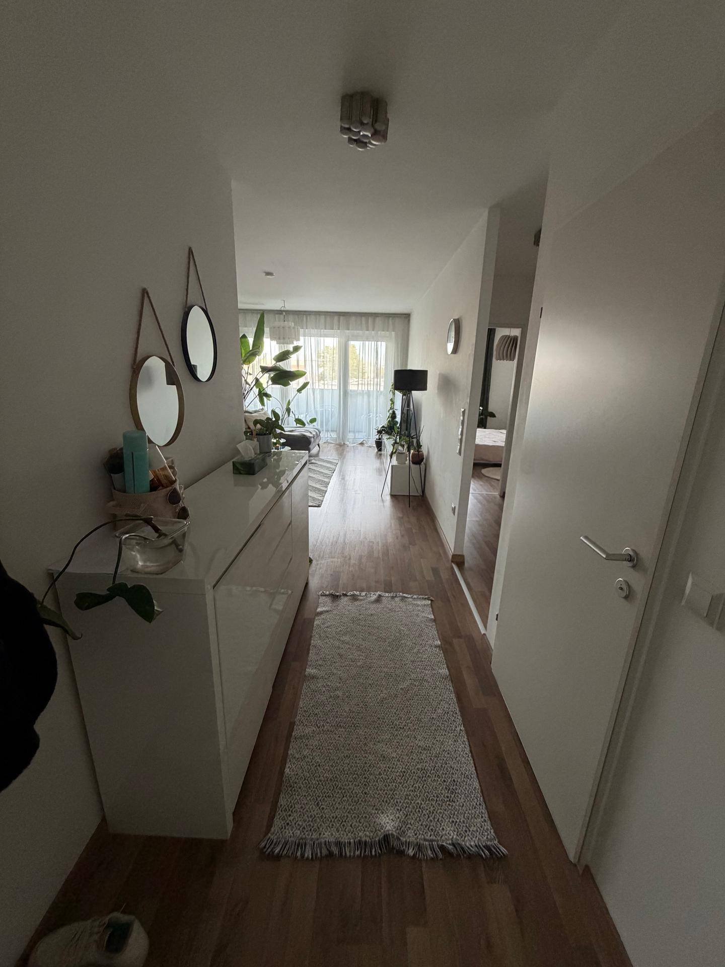 Heller Flur mit modernem Sideboard, runden Spiegeln und Holzboden.