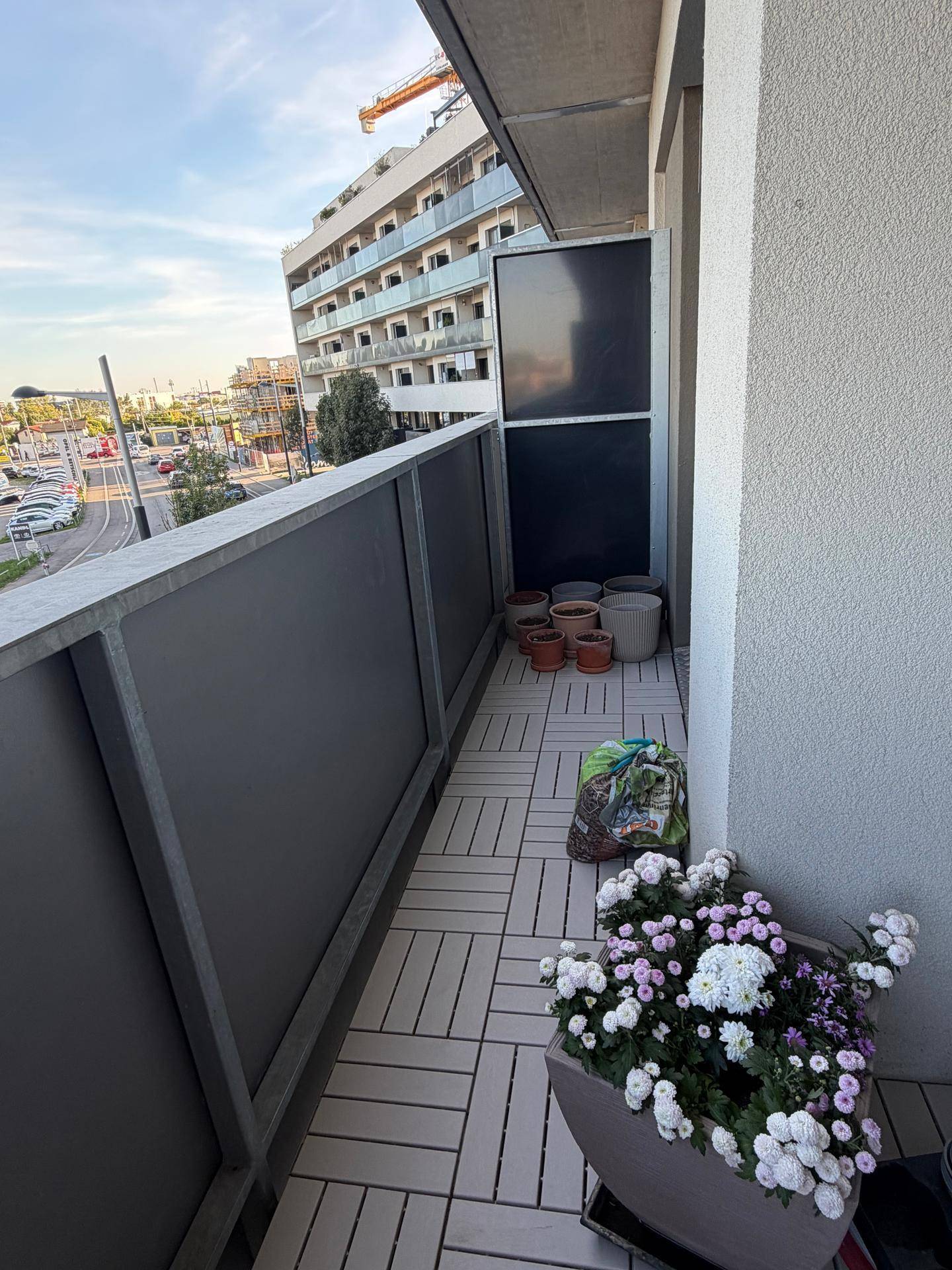 Langer Balkon mit Pflanzen und Ausblick auf die umliegenden Gebäude und die Straße.