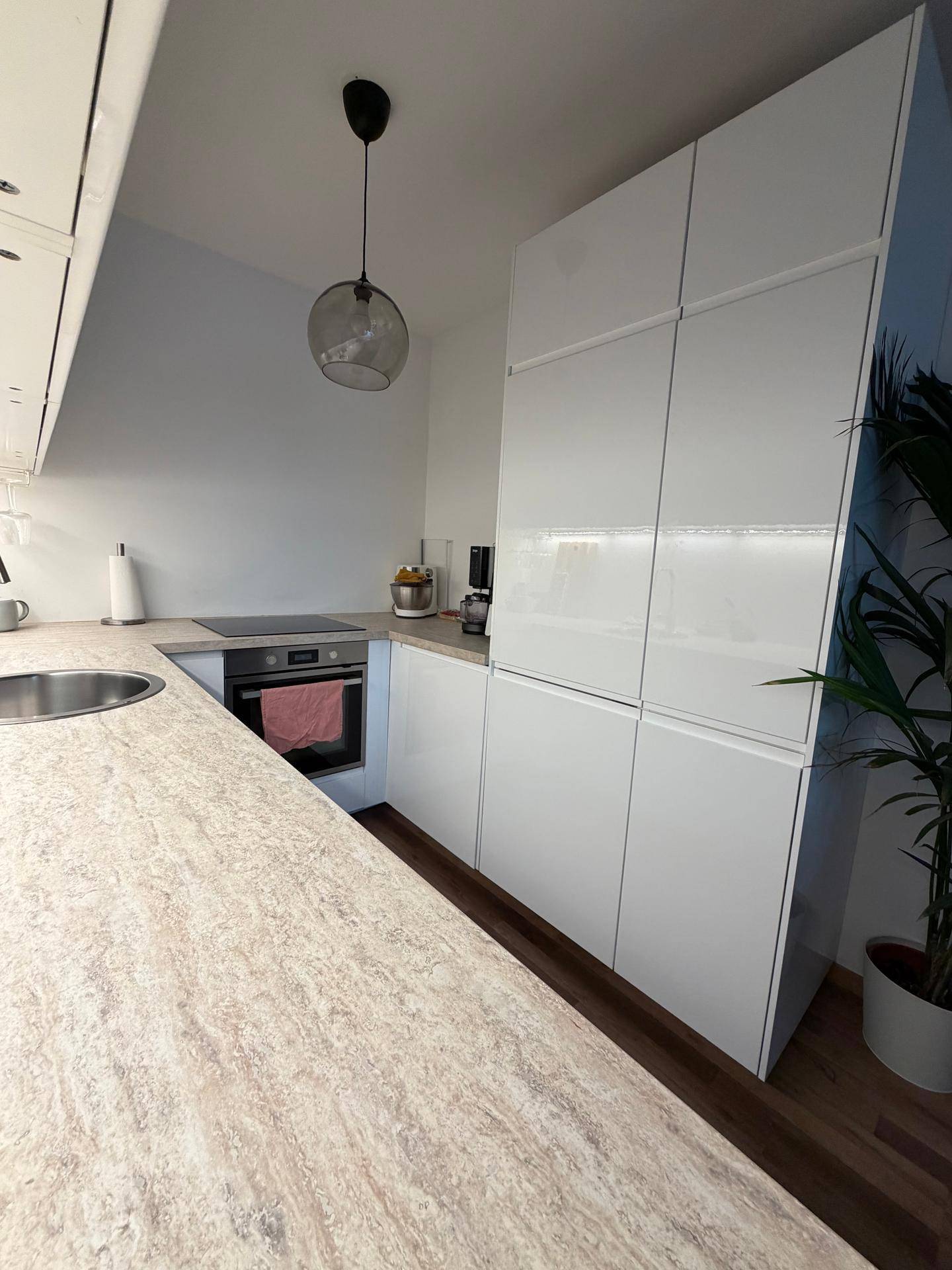 Helle Küche mit weißen Hochglanzschränken, Kochfeld und integriertem Backofen.