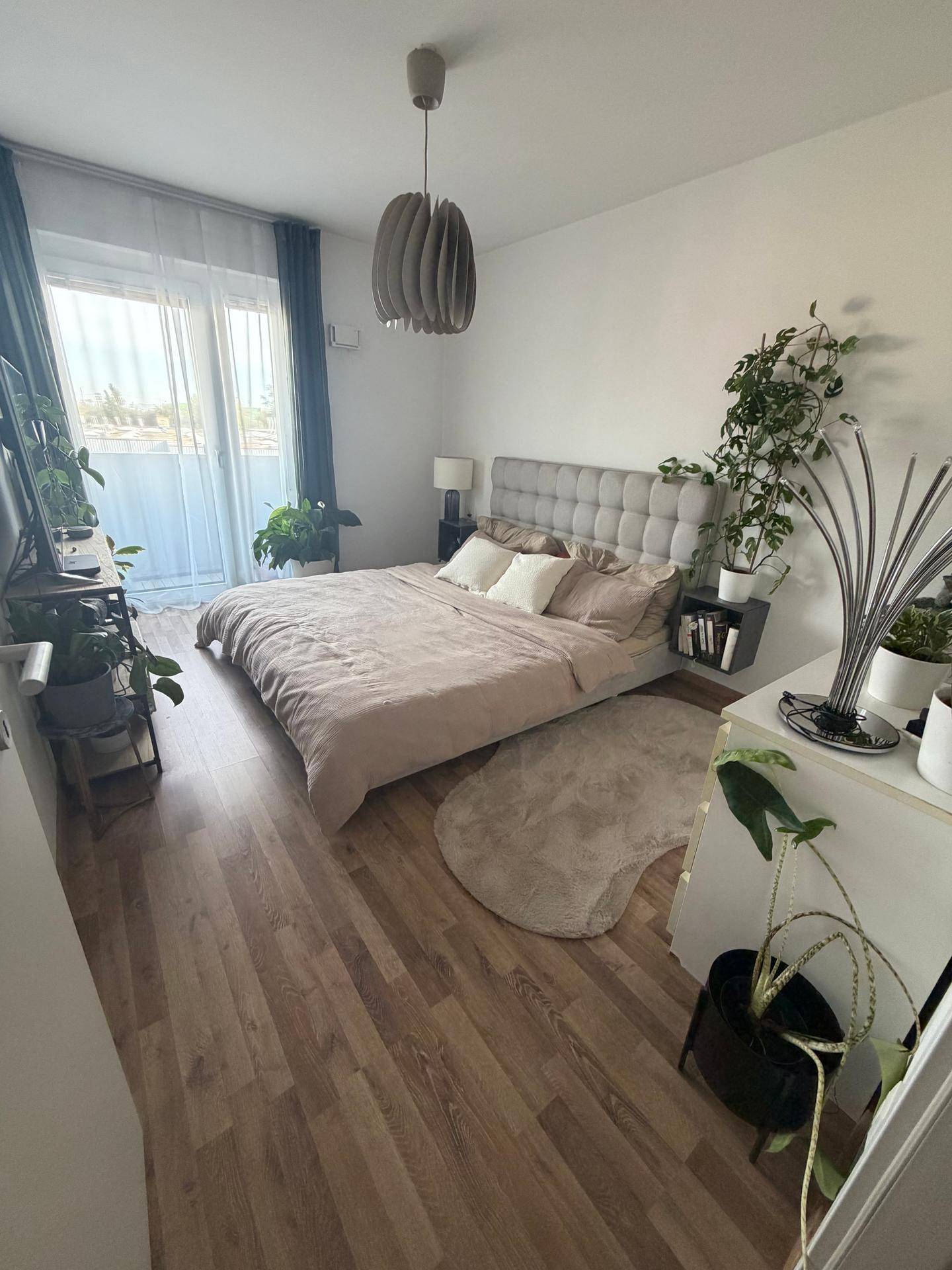 Gemütliches Schlafzimmer mit großem Bett, vielen Pflanzen und Zugang zum Balkon.