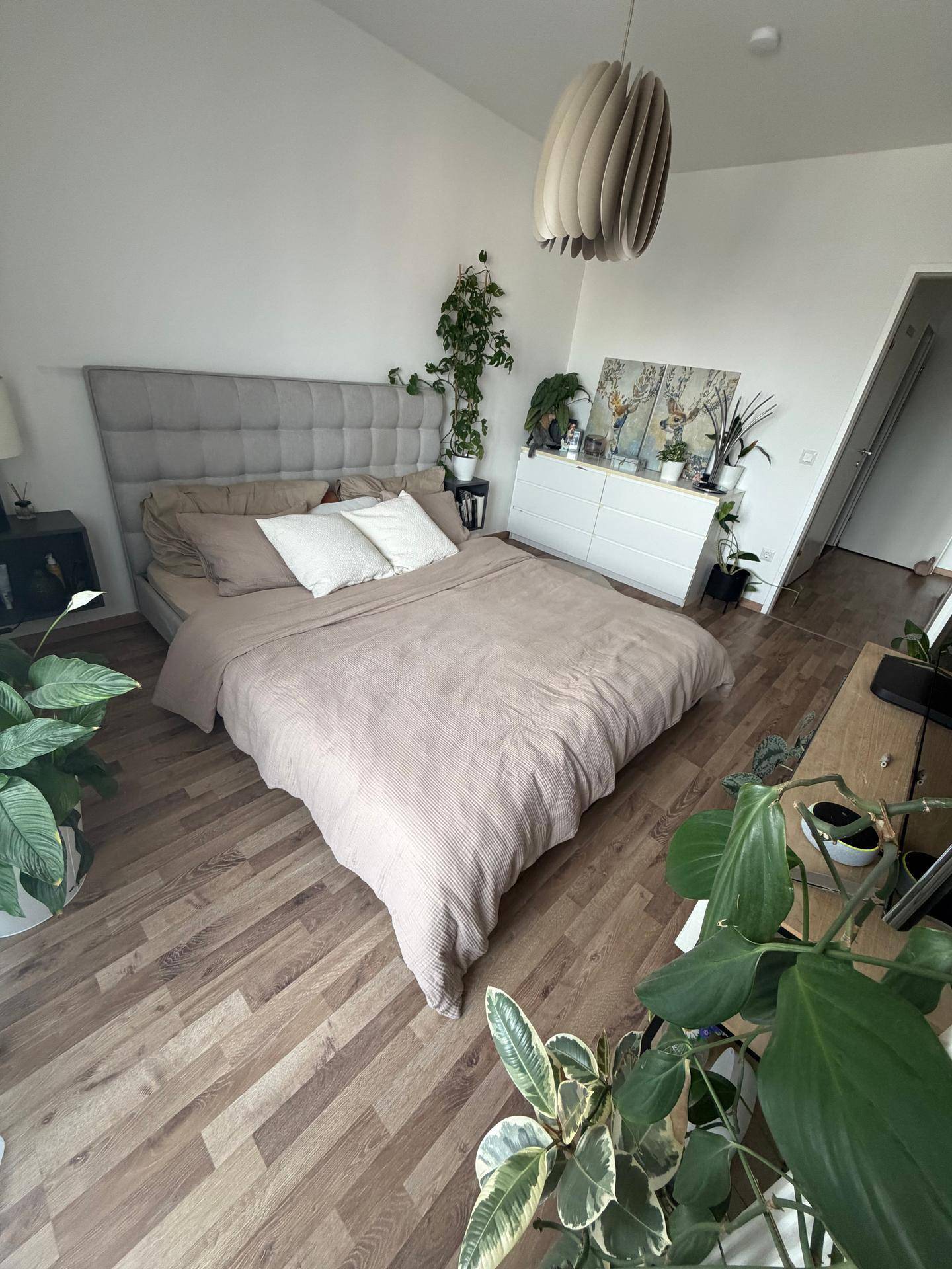 Helles Schlafzimmer mit bequemen Bett, Kommode und dekorativen Grünpflanzen.