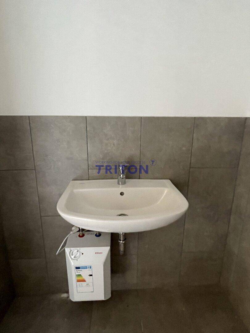 Waschbecken mit Untertischgerät und Fliesen an der Wand in einem Sanitärraum.